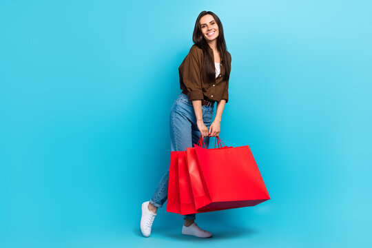 Full size body photo of dreamy good mood shopaholic hispanic young girl holding red bargains shiny isolated on blue color background