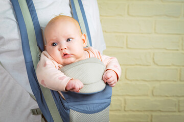 Portrait of a cute little baby girl in a sling looking at the camera.