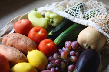 Reusable mesh bag with seasonal fruit and vegetable on wooden background. Late summer or early autumn. Selective focus.