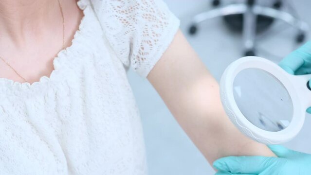 a female dermatologist using a medical magnifying glass in the clinic examines the patient's skin.