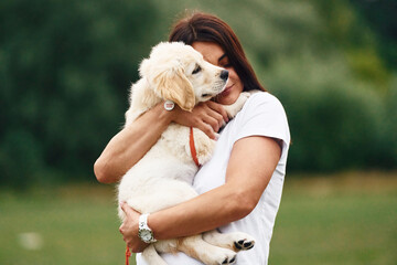 Puppy is in hands. Woman with cute little golden retriever dog is on the green field