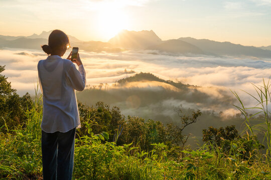 Female tourists carry backpacks, travel, hike, hold smartphones and take photos of the sea of mist from the mountain top and feeling free, good weather in the morning, weekend holidays.