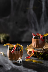 Halloween treats, scary chocolate mousse with gummy worms in glasses on dark festive background....