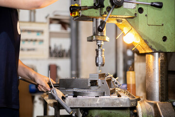 Professional worker working on drilling a steel piece with an industrial machine in a metal factory workshop. Mechanics machinery.
