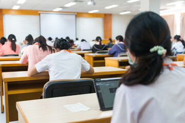 Rear view of university students concentrate on doing examinations via tablet and smartphone in the...