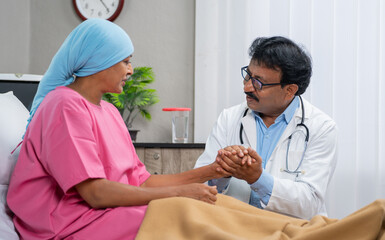Indian doctor consoling cancer patient by giving confidence while holding hands at hospital -...