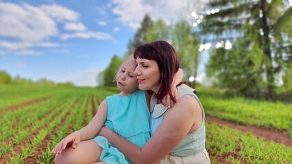 Naklejka na ściany i meble Happy mother and daughter enjoying rest, playing and fun on nature in green field. Woman and girl resting outdoors in summer and spring day