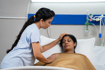 Indian daughter feeling bad or worried for sick sleeping mother at hospital ward- concept of family caring, medical treatment and relationship bonding