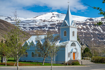 Blue wooden Church at Seydisfjordur, Iceland, view from the side with snow mountains in the...