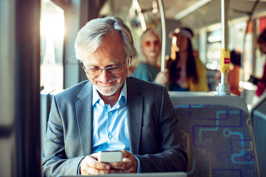 Senior Caucasian businessman using his smartphone while going to work on the bus