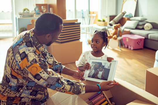 Young African American girl showing her father the picture of them after opening boxes in their new apartment