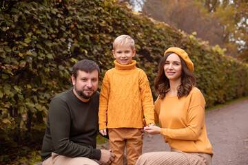 Fototapeta premium Portrait of a beautifully dressed family, mom in an orange beret, dad and 7 year old son in an autumn park.