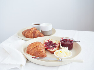 Croissant with butter and raspberry jam, served on a white tablecloth table with a cup of coffee.