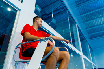 young professional umpire in the game of tennis sitting on the observation tower and watching the...