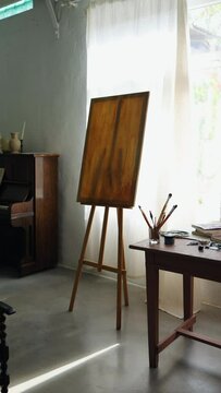 wooden empty easel near window in room with retro piano and table with dice and paints. artist's room vertical video