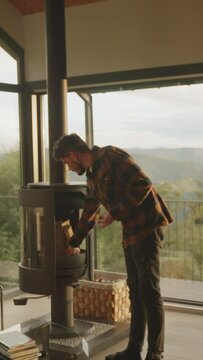 Chico enciende chimenea en sal&oacute;n con ventanal, ofreciendo vistas a monta&ntilde;as frondosas. Momento acogedor y panor&aacute;mico