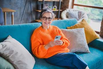 Photo of charming cheerful person sit cozy couch use smart phone texting typing blog post modern flat indoors
