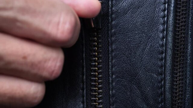 man's hand unzips a leather jacket close-up