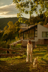 Fototapeta premium Chica pasea con cachorro golden retriever en jardín de casa montañesa. Momentos felices en un paisaje majestuoso.