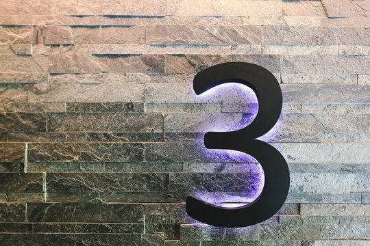 Dark  Neon Font with fluorescent purple tubes  Number 3 on the dark brown brick wall.  Night Show Alphabet.