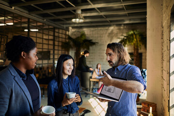Young Caucasian male designer showing the progress of his work on a laptop to his colleagues