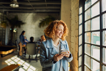 Young Caucasian woman drinking coffee and using a smartphone in a startup company office