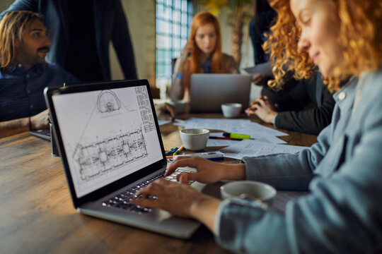 Young Caucasian Female Designer Working On Building Plans On Her Laptop In A Startup Company Office