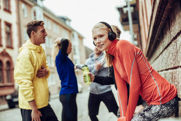 Young fit Caucasian woman listening to music on her headphones while getting ready to run with her friends in the city