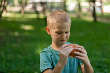 the boy holds in his hands a hamburger that he didn’t like. displeasure on the face. dressed with a green t-shirt