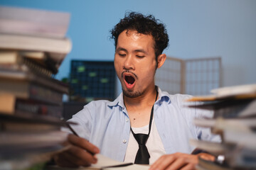 Asian Male manager, employee is yawning during late work at midnight or night time at office....
