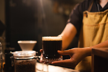 Fototapeta na wymiar SME or start up business owner is serving Black coffee or americano in loft aroma coffee shop or cafe counter bar. Concept of slow bar, coffee caffeine. Black and brown style. Preparation of coffee.