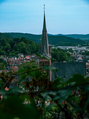 A Church tower made of red stones with a green roof in a German village with leaves as a frame