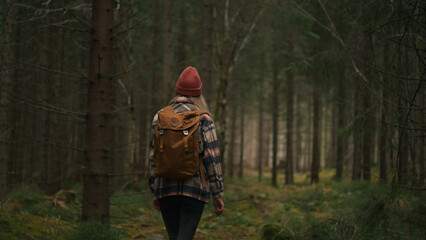 Back view of active healthy caucasian woman with backpack traking in wood