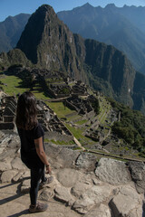 Young woman with long flowing hair, wearing sportswear, with her back turned looking at the archeological site of Machupicchu, Peru. 