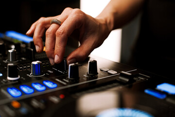 Close up portrait of female disc jockey hand mixing tracks on professional sound mixer, playing...
