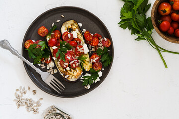 Roasted eggplant, tomatoes, fresh cheese, sunflower seedes, and parsley herbs in plate on white table top view