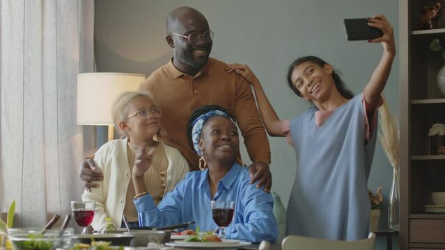 Cheerful African American family posing together for smartphone camera while taking group selfie on holiday dinner at home