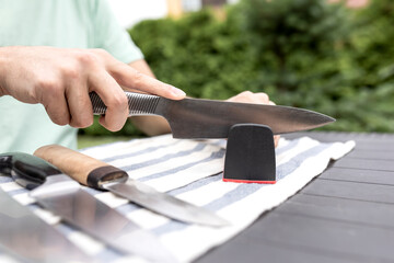 Fototapeta na wymiar Close-up photo of man sharpening knives with special knife sharpener outdoor