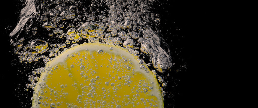 Underwater of freshly squeezed sweetened lemonade which raw lemons slice falling in soda water against dark blue or black background. Close up lemonade or Highball lemon cocktail cold refreshing drink