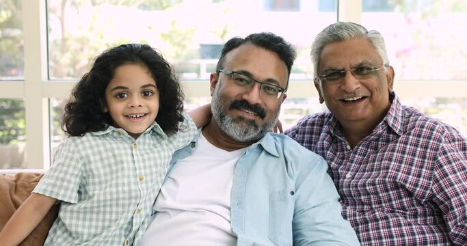 Close up portrait of happy Indian little boy, mature grandfather and old great-grandfather. Multi-generational family resting on couch smile look at camera, feeling love, showing protection and care