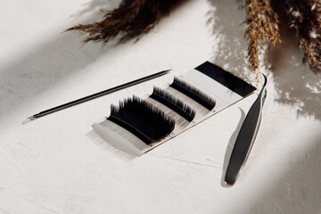 Composition of set of eyelashes different in shape and length, tweezers and applicator on light background MOCKUP.