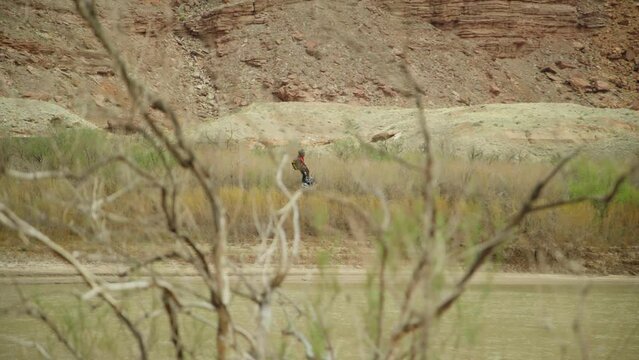 Man in jet pack flies down river past trees and bushes. 