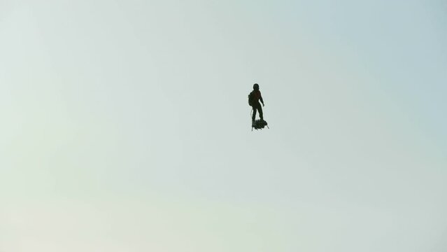 Sunrise as man flies in sky with jet pack