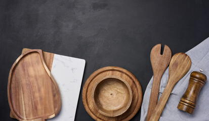 Empty bowl and wooden spoons on a black table, top view