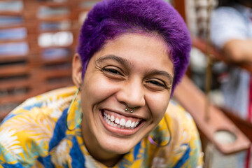 Close-up portrait of a bisexual woman with short purple hair and a big happy smile looking at the...