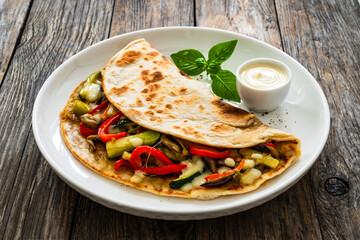 Italian piada wraps - piadina filled with fried vegetables and mozzarella cheese on wooden table
