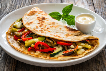 Italian piada wraps - piadina filled with fried vegetables and mozzarella cheese on wooden table
