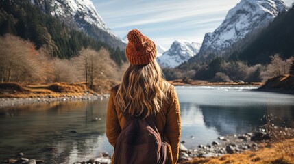 Female hiker in winter hat enjoying calm lake view. - obrazy, fototapety, plakaty