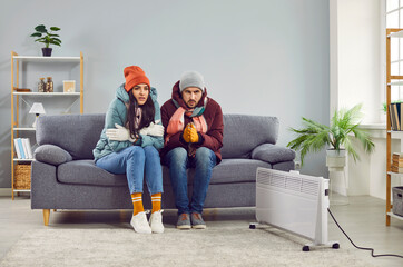 Freezing people in winter jackets sitting on sofa at home. Sad warmly closed husband abd wife...