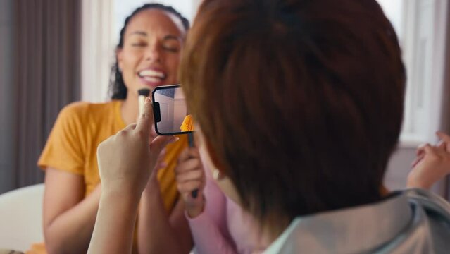 Female friends at home having fun recording video on phone miming singing song into make up brushes - shot in slow motion